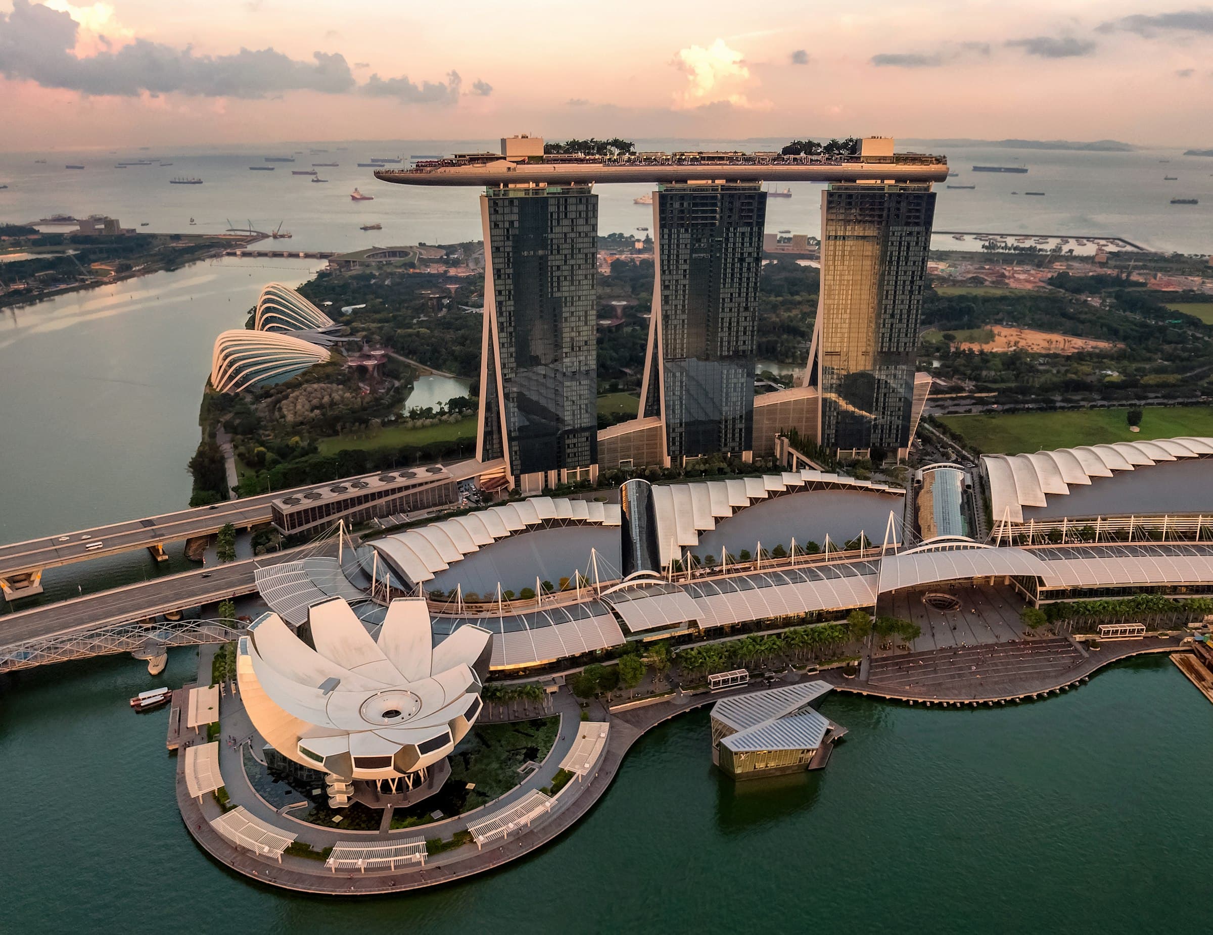 Marina Bay from the air at dusk: the three towers of Marina Bay Sands, the ArtScience Museum, and Gardens by the Bay behind them